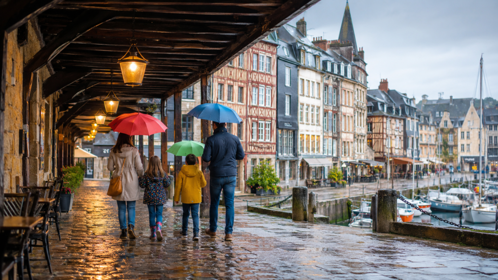 Famille se promenant sous des parapluies sur le port de Honfleur pendant une averse légère.